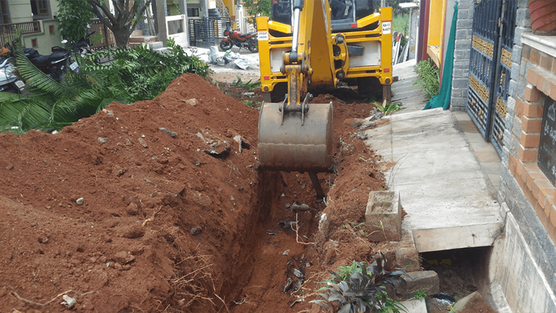 Excavator Digging A Trench Beside A Residential Building Png
