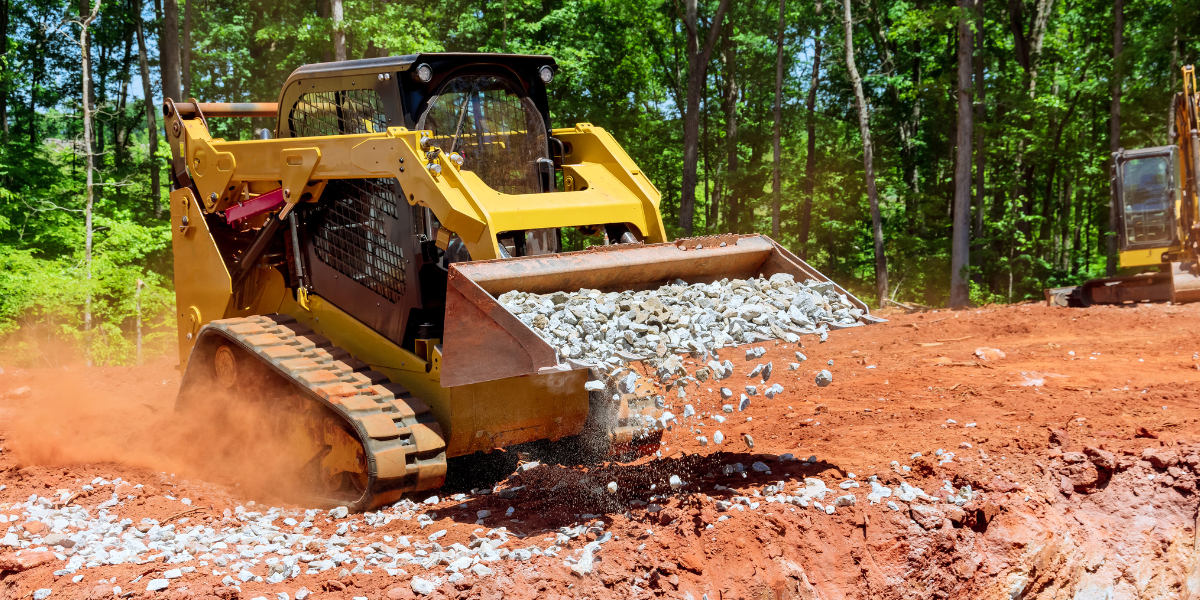 Skid steer loader spreading crushed stone on a construction site.