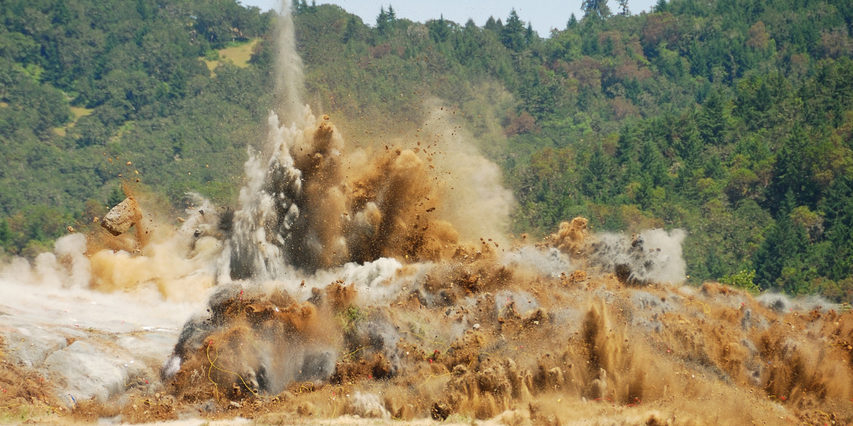 Controlled rock blast sending dirt and debris into the air on a hillside