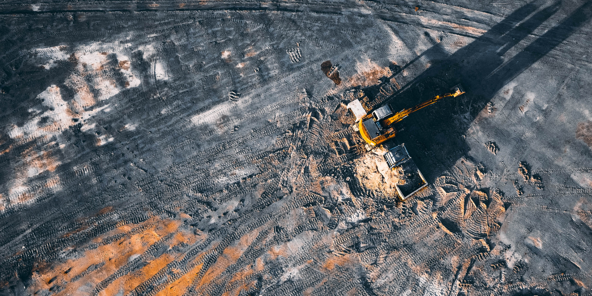 Excavator digging on a large construction site with visible tire tracks and soil patterns