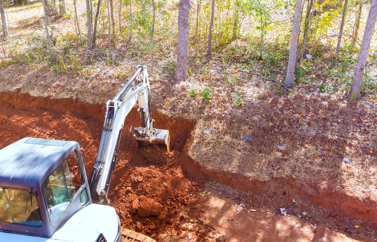 Excavator digging a deep trench in red clay soil